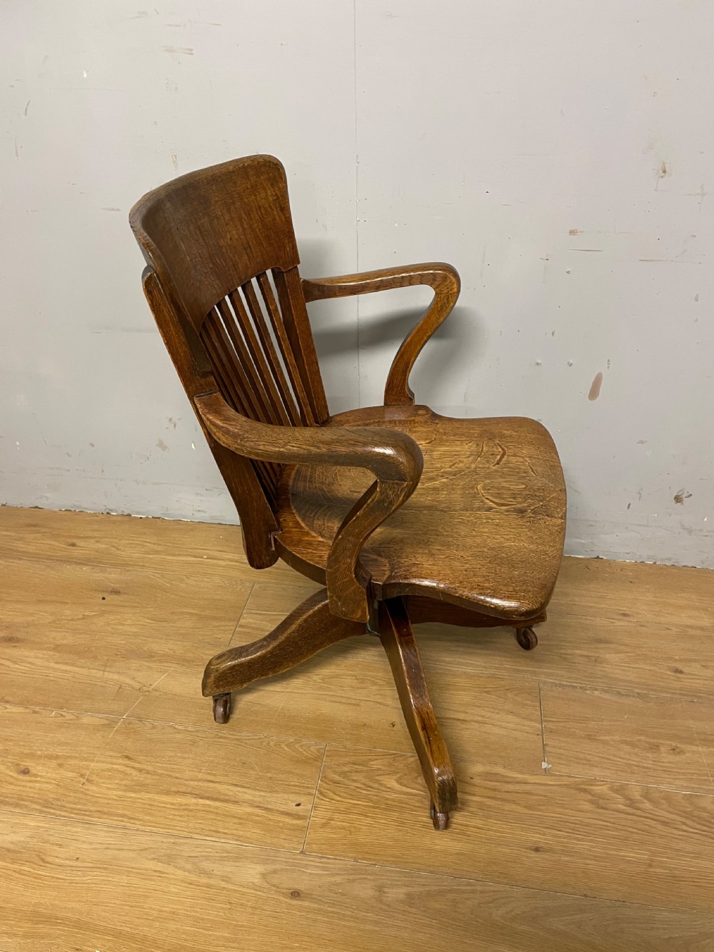 An Edwardian solid oak revolving and tilting office chair with a curved backrest, vertical spindles, and castors. View VII