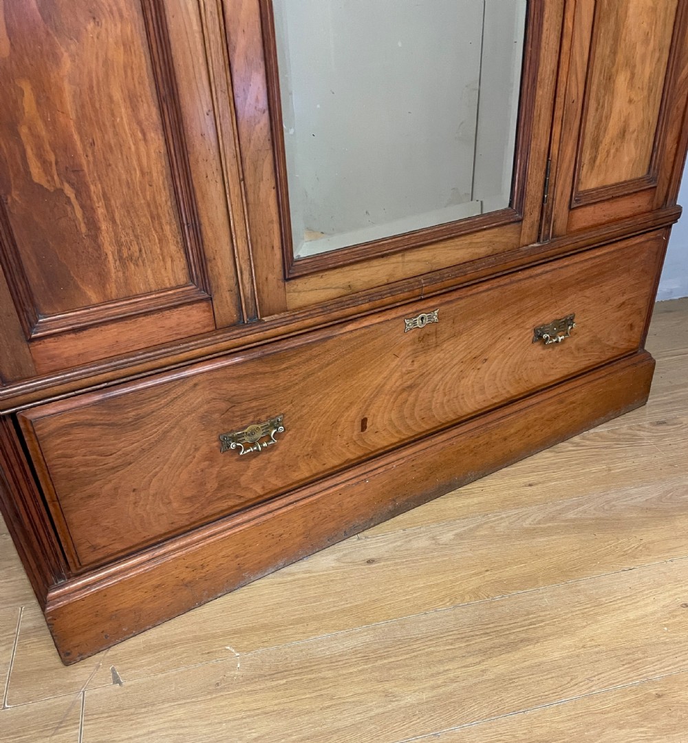 A late 19th-century Arts and Crafts satin walnut wardrobe featuring a central mirrored door, carved foliate panels, and a single base drawer. View III