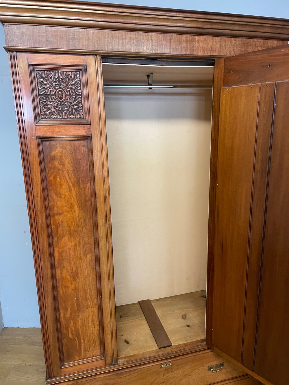 A late 19th-century Arts and Crafts satin walnut wardrobe featuring a central mirrored door, carved foliate panels, and a single base drawer. View VII