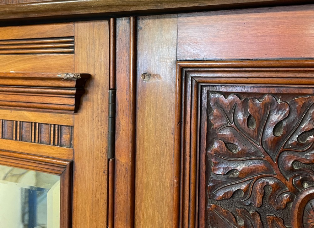A late 19th-century Arts and Crafts satin walnut wardrobe featuring a central mirrored door, carved foliate panels, and a single base drawer. View IX