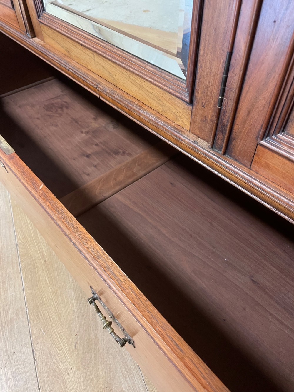 A late 19th-century Arts and Crafts satin walnut wardrobe featuring a central mirrored door, carved foliate panels, and a single base drawer. View XI