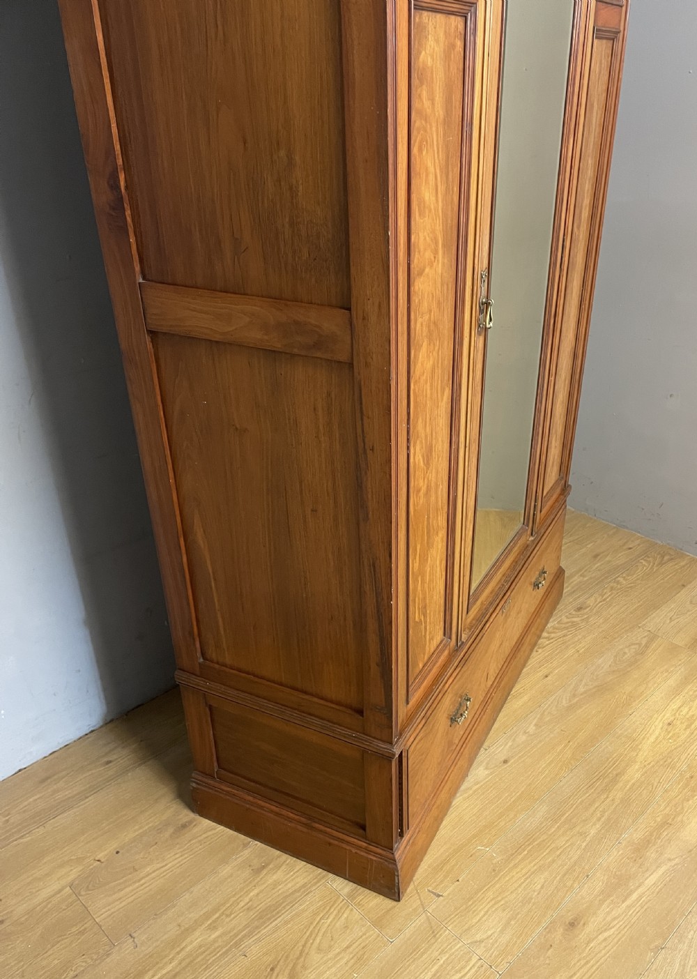 A late 19th-century Arts and Crafts satin walnut wardrobe featuring a central mirrored door, carved foliate panels, and a single base drawer. View XIII