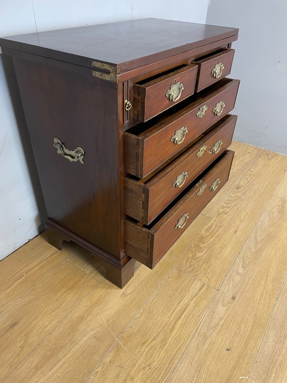 A 19th-century mahogany bachelors chest of drawers featuring a fold-over top, brass drop handles, side carrying handles, and bracket feet. View III