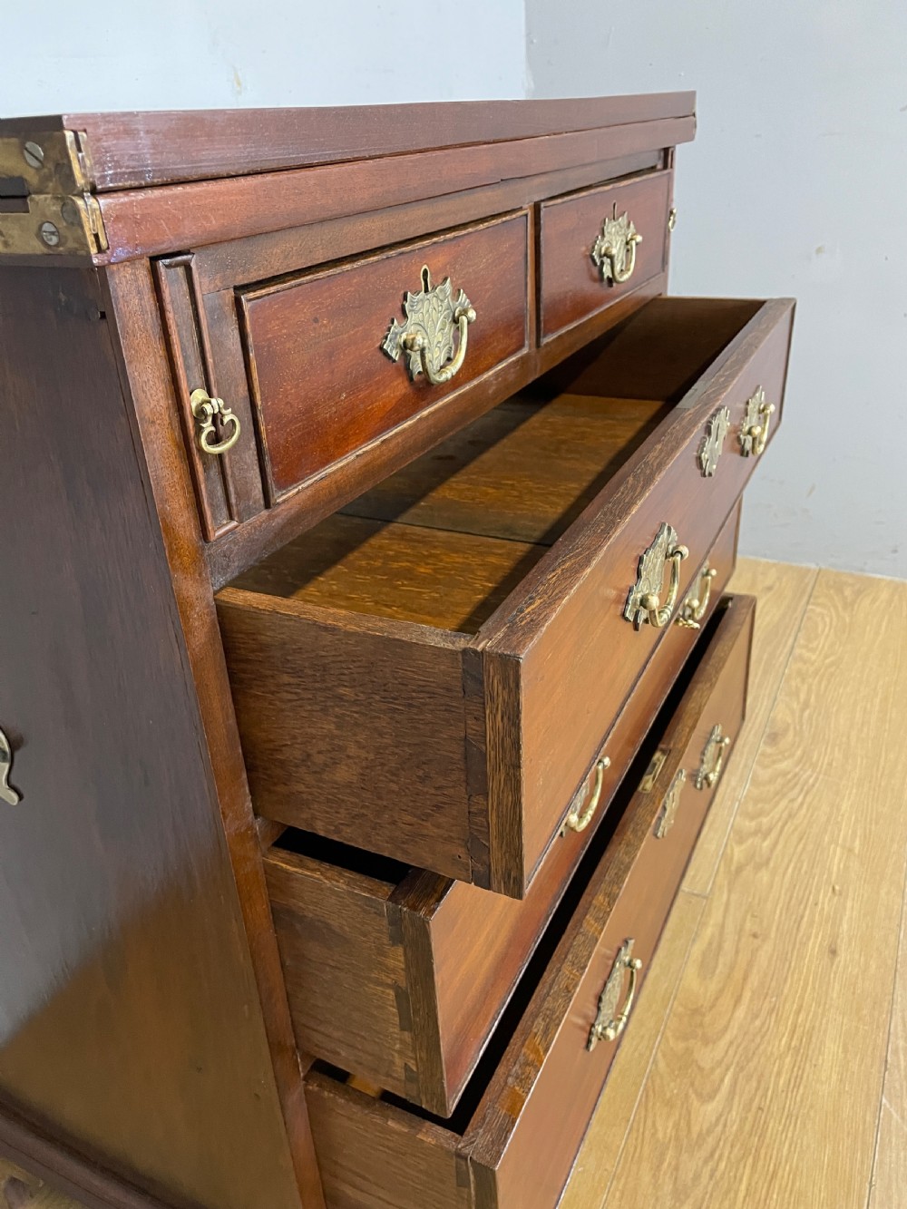 A 19th-century mahogany bachelors chest of drawers featuring a fold-over top, brass drop handles, side carrying handles, and bracket feet. View V