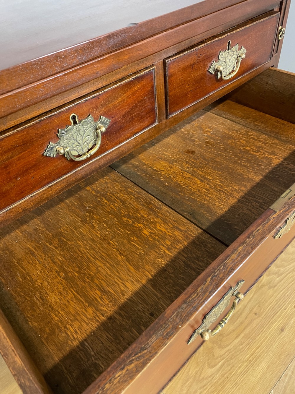A 19th-century mahogany bachelors chest of drawers featuring a fold-over top, brass drop handles, side carrying handles, and bracket feet. View VI