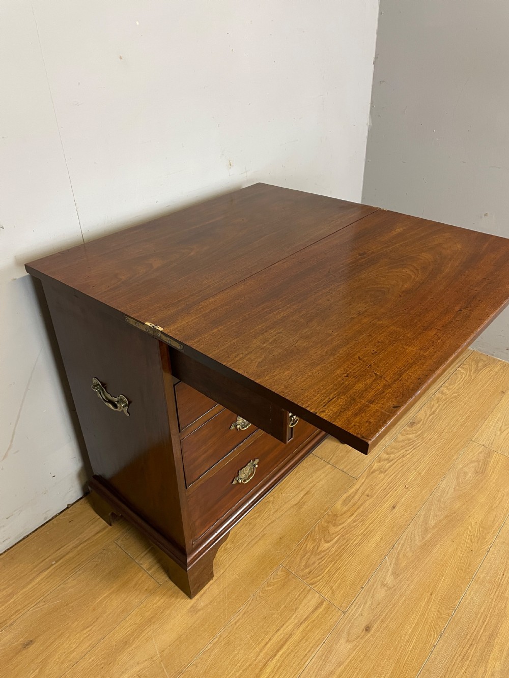 A 19th-century mahogany bachelors chest of drawers featuring a fold-over top, brass drop handles, side carrying handles, and bracket feet. View VII