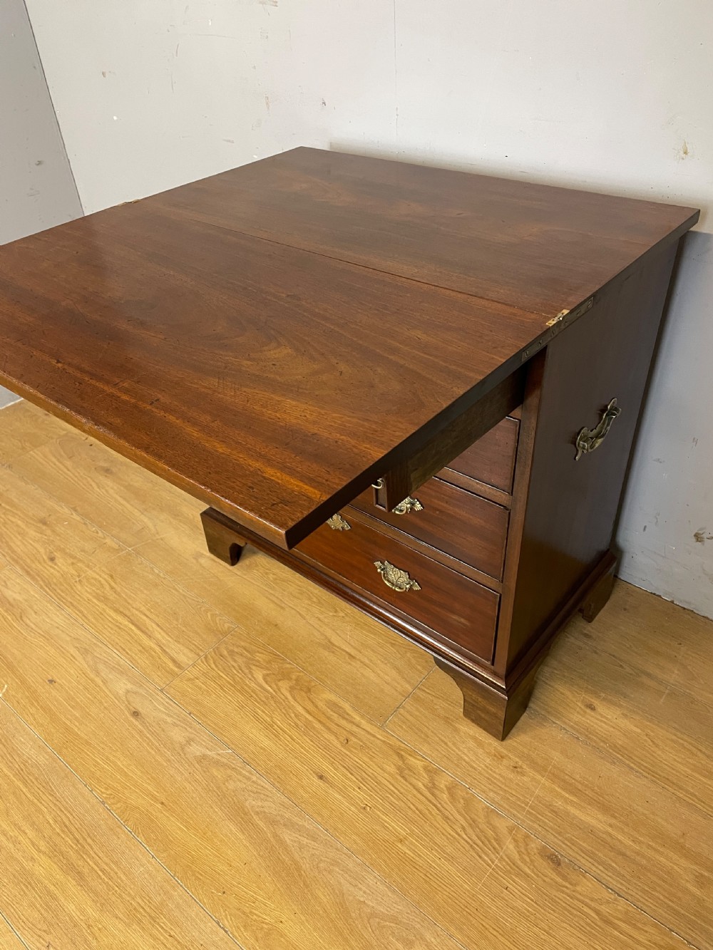 A 19th-century mahogany bachelors chest of drawers featuring a fold-over top, brass drop handles, side carrying handles, and bracket feet. View IX