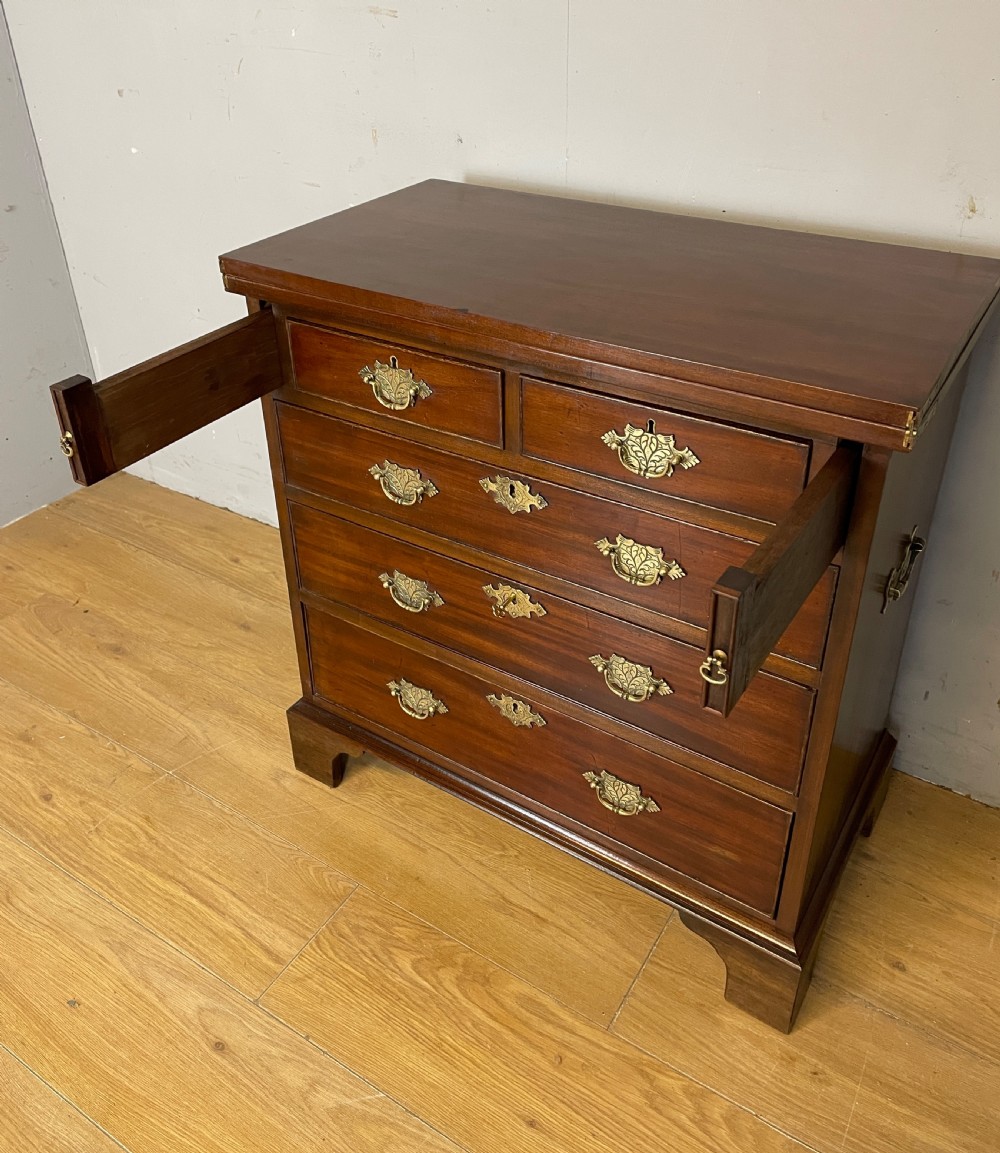 A 19th-century mahogany bachelors chest of drawers featuring a fold-over top, brass drop handles, side carrying handles, and bracket feet. View X