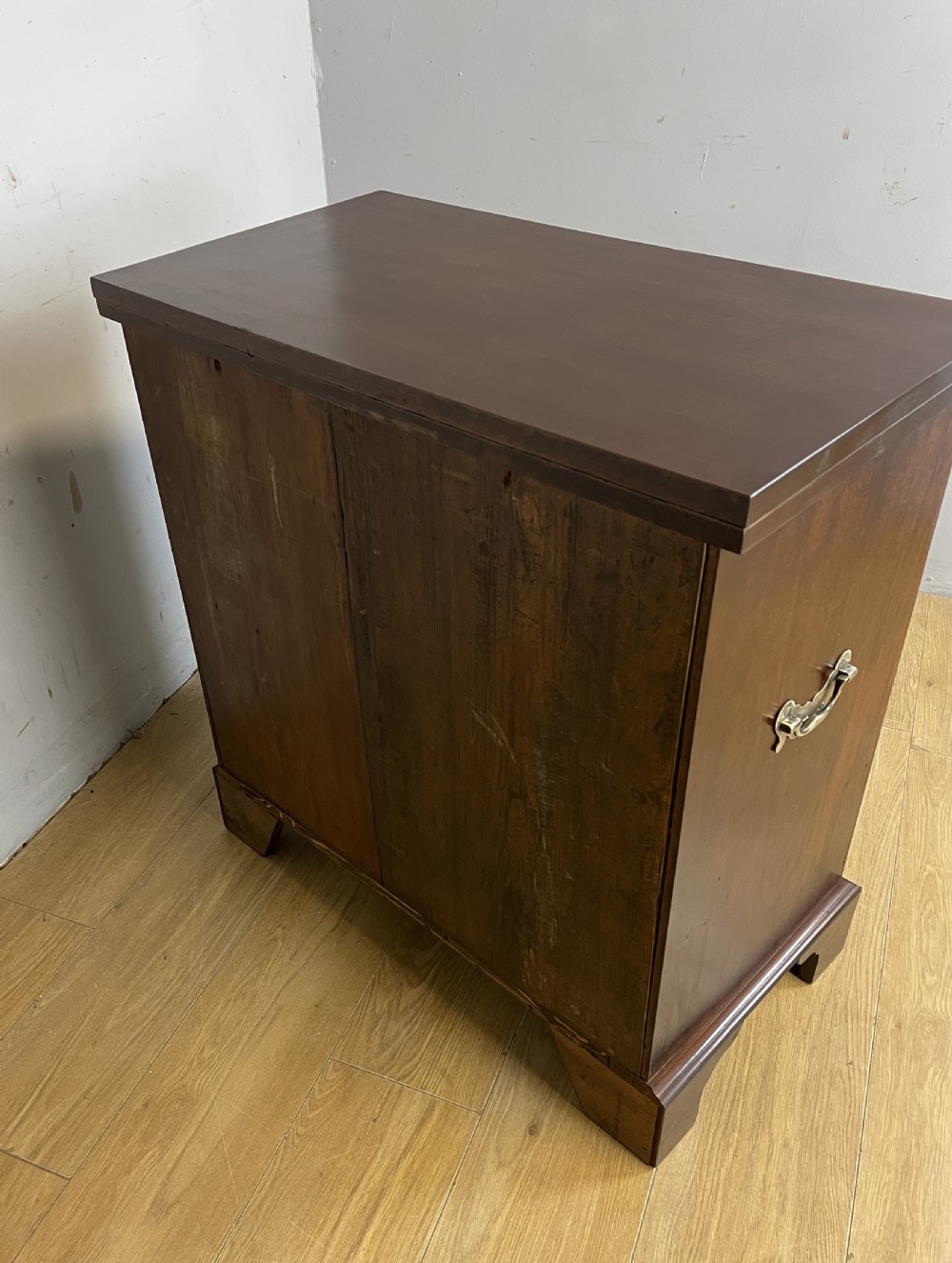 A 19th-century mahogany bachelors chest of drawers featuring a fold-over top, brass drop handles, side carrying handles, and bracket feet. View XII