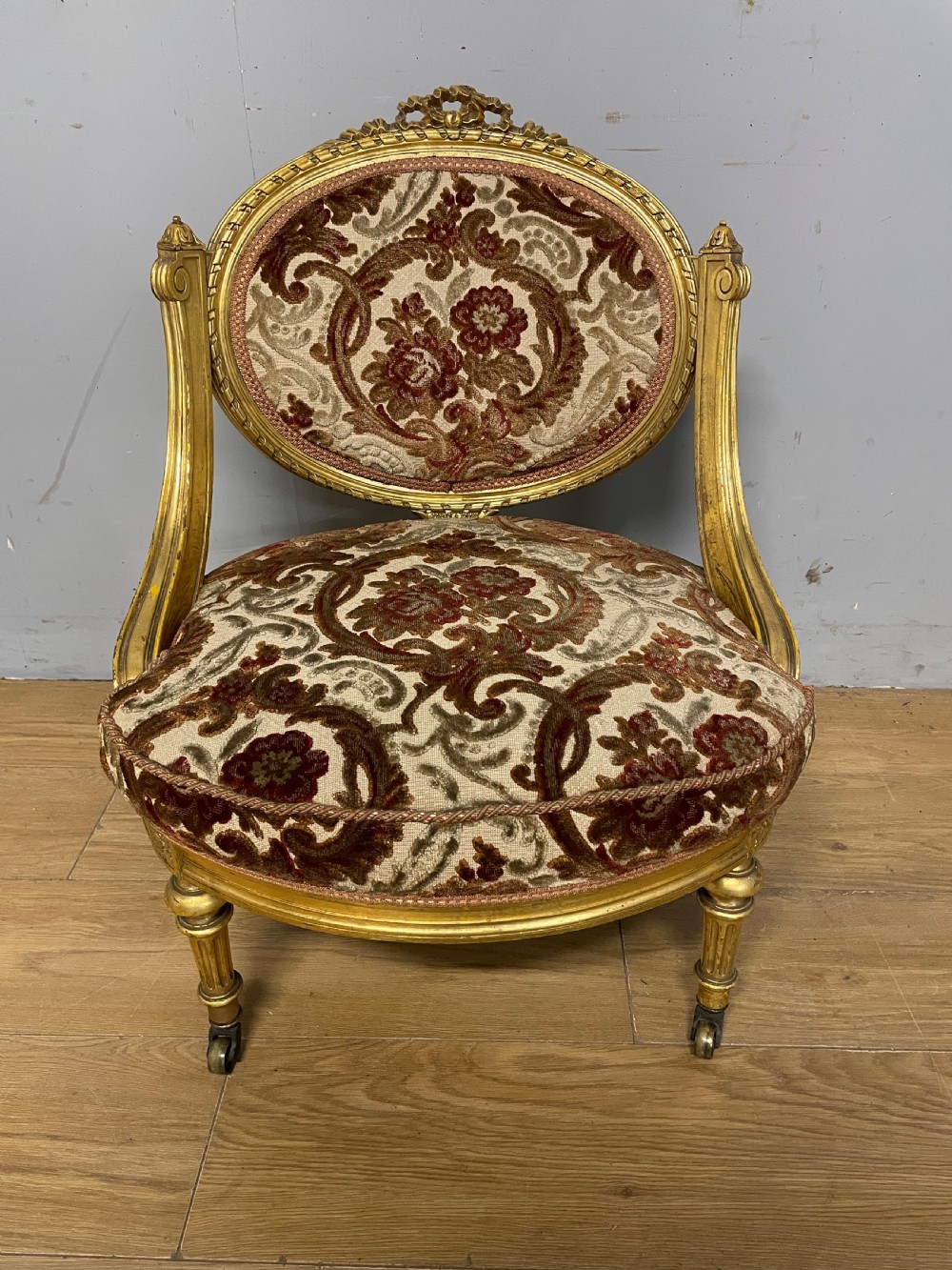 A 19th-century carved giltwood nursing chair featuring patterned burgundy velvet upholstery, an oval backrest, and short turned legs with castors. View II