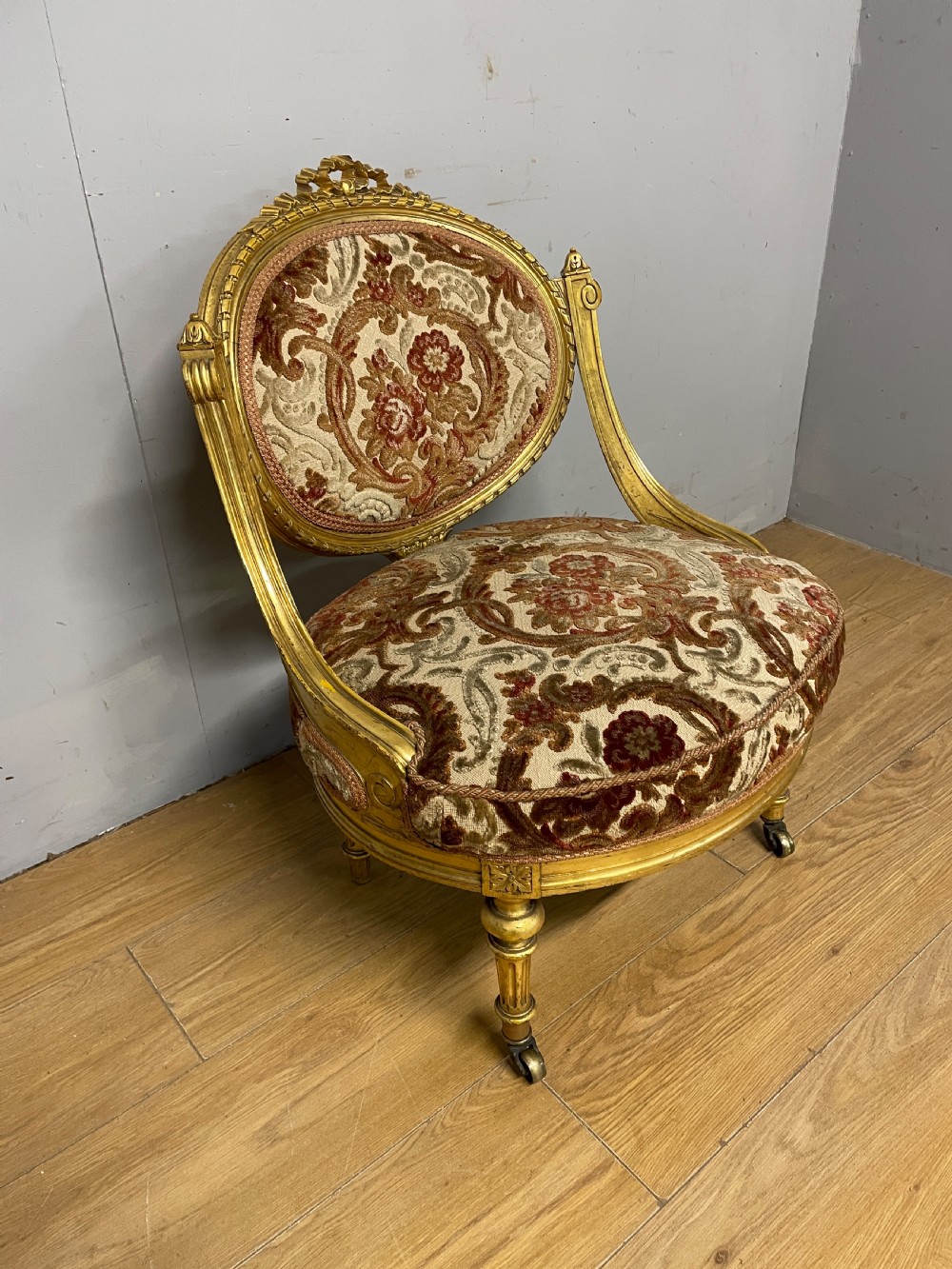 A 19th-century carved giltwood nursing chair featuring patterned burgundy velvet upholstery, an oval backrest, and short turned legs with castors. View III