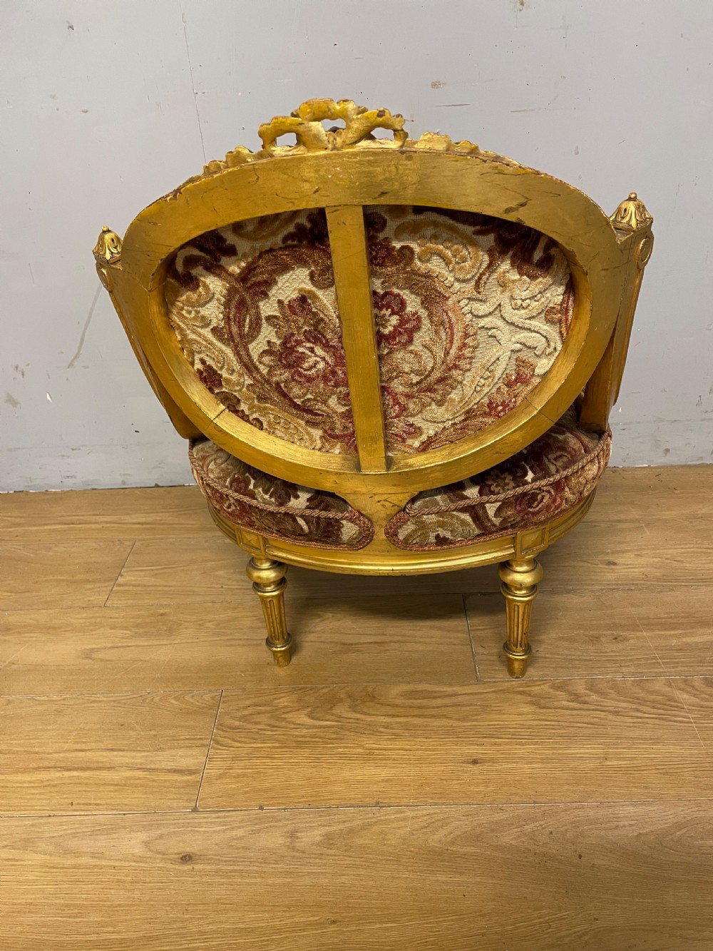 A 19th-century carved giltwood nursing chair featuring patterned burgundy velvet upholstery, an oval backrest, and short turned legs with castors. View VII