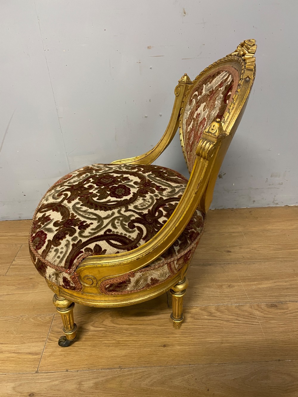 A 19th-century carved giltwood nursing chair featuring patterned burgundy velvet upholstery, an oval backrest, and short turned legs with castors. View VIII