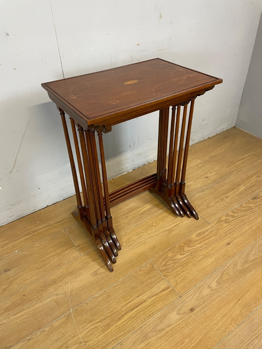 An Edwardian nest of four rectangular mahogany tables featuring satinwood floral line inlay and slender turned legs resting on trestle feet.