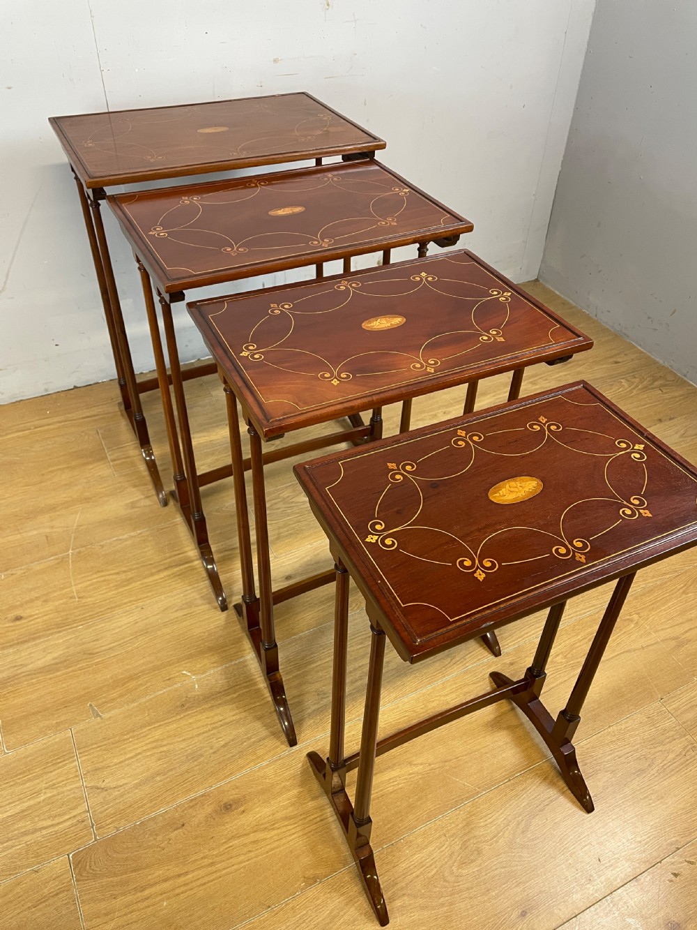 An Edwardian nest of four rectangular mahogany tables featuring satinwood floral line inlay and slender turned legs resting on trestle feet. View V