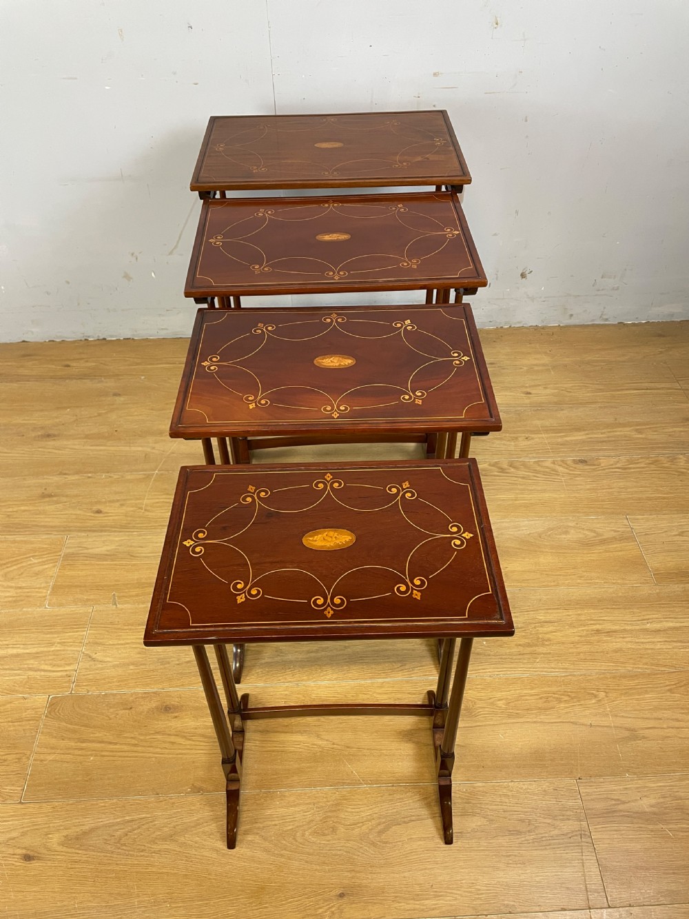 An Edwardian nest of four rectangular mahogany tables featuring satinwood floral line inlay and slender turned legs resting on trestle feet. View VI