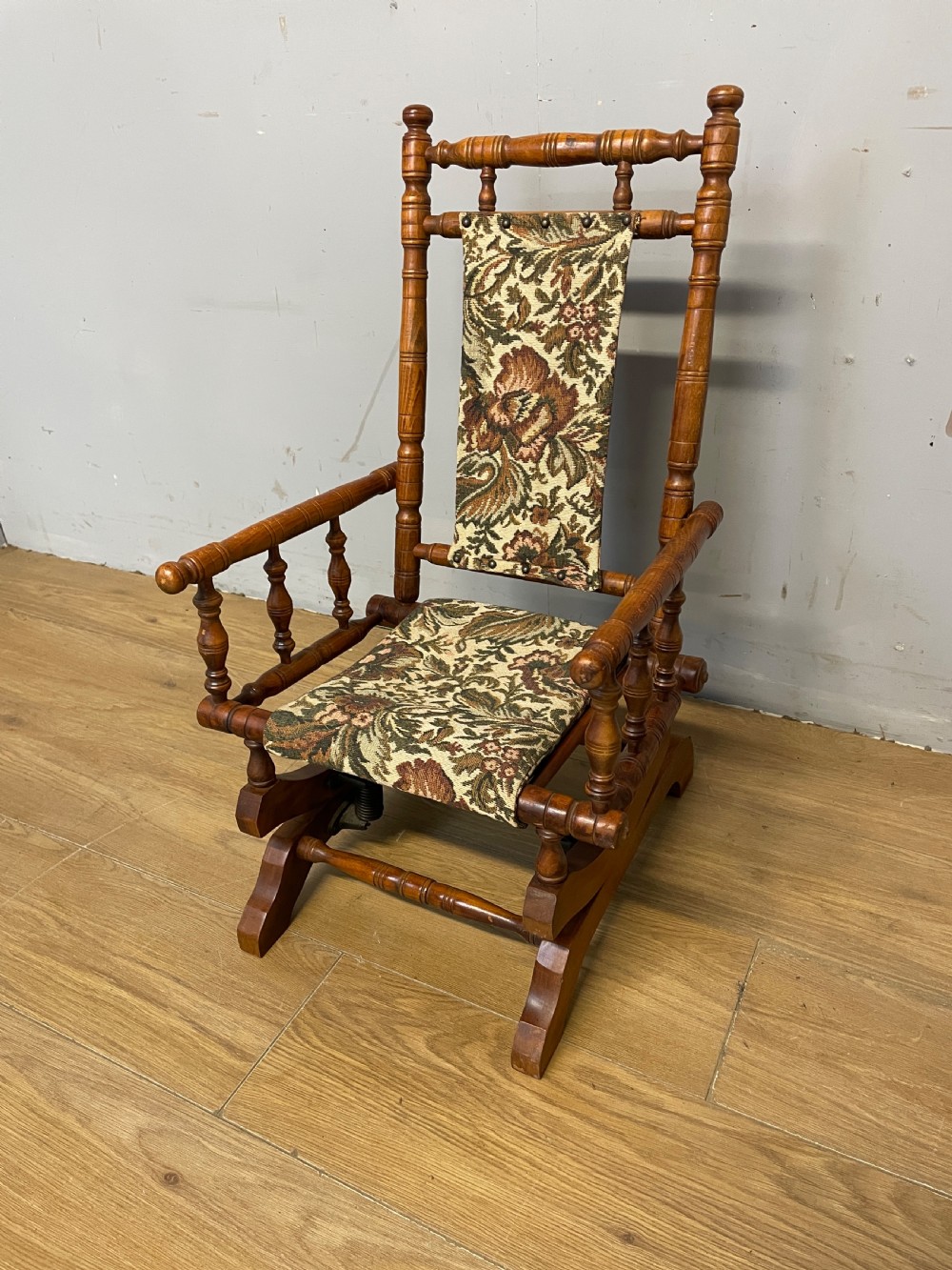 A 19th-century childs American platform rocking chair made of turned wood with floral tapestry fabric on the seat and backrest.