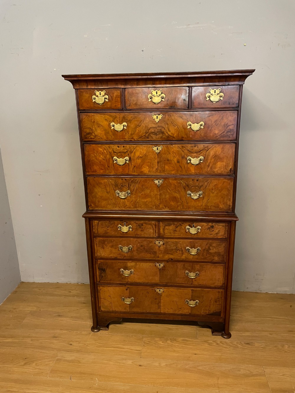 A nineteenth-century burr walnut chest on chest with multiple drawers, brass drop handles, keyhole escutcheons, and bracket feet.