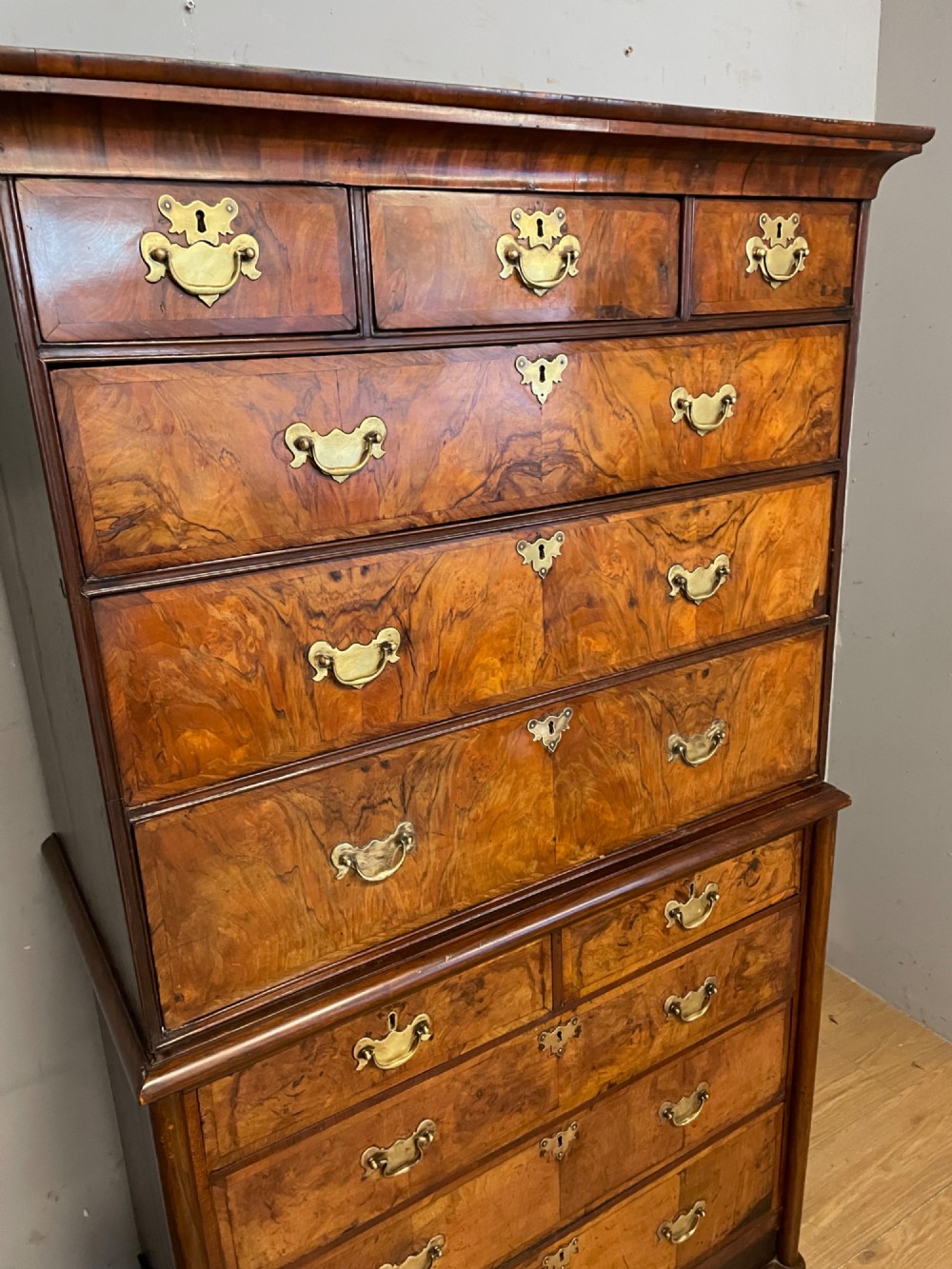 A nineteenth-century burr walnut chest on chest with multiple drawers, brass drop handles, keyhole escutcheons, and bracket feet. View IV
