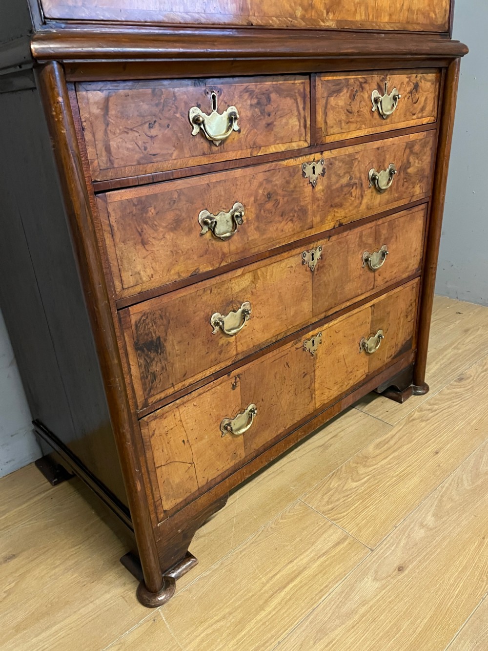 A nineteenth-century burr walnut chest on chest with multiple drawers, brass drop handles, keyhole escutcheons, and bracket feet. View V