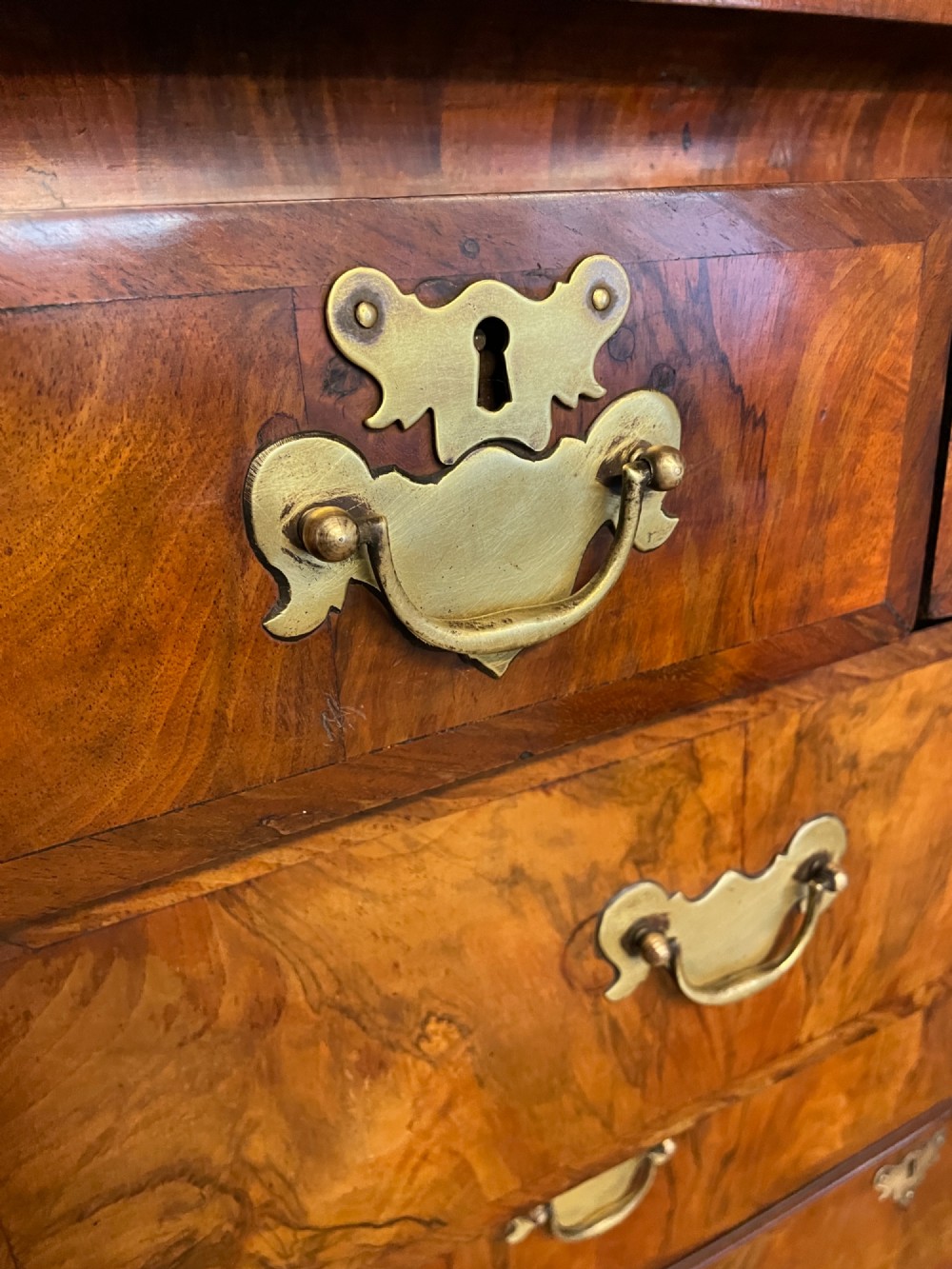 A nineteenth-century burr walnut chest on chest with multiple drawers, brass drop handles, keyhole escutcheons, and bracket feet. View VII