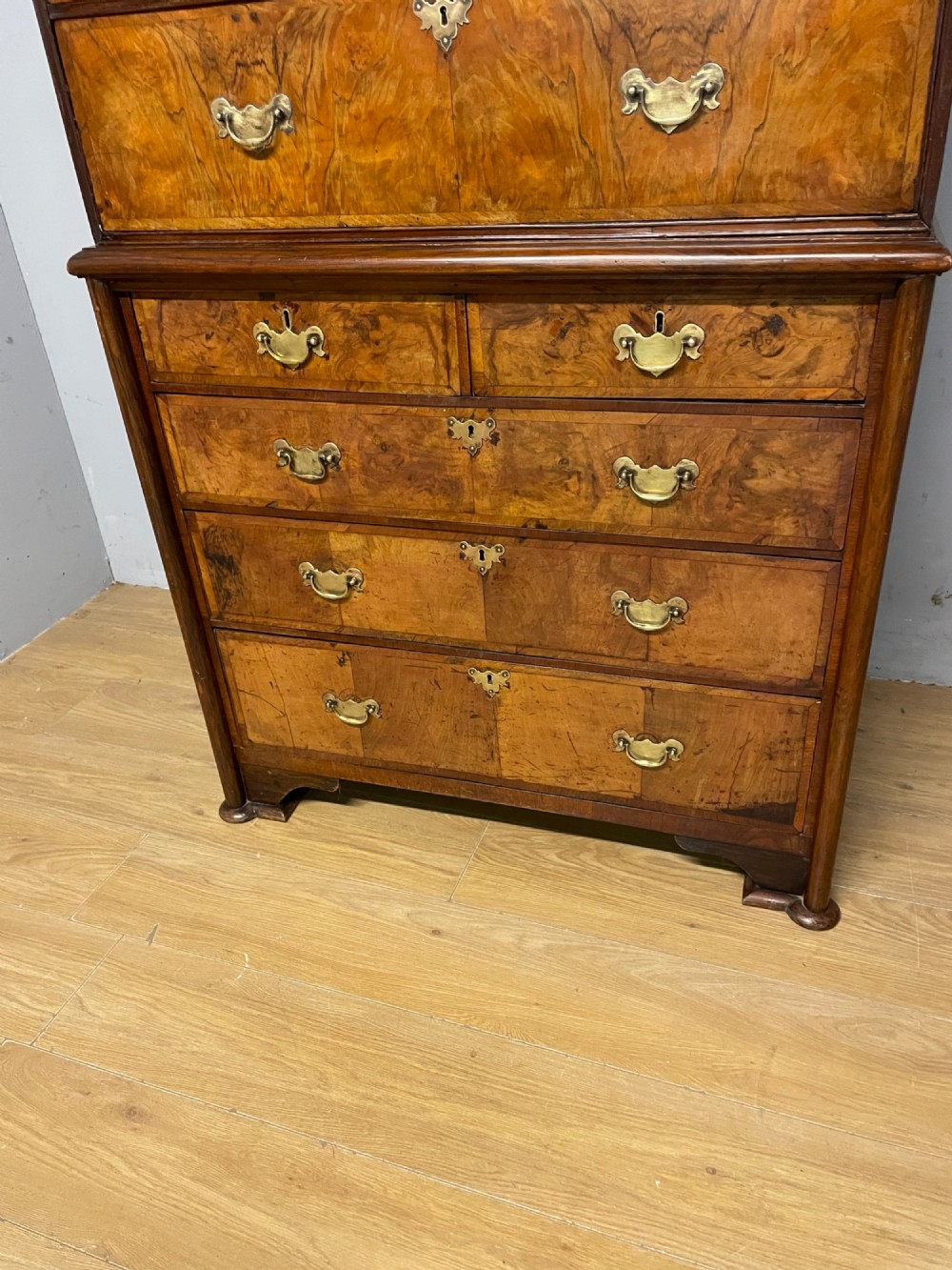 A nineteenth-century burr walnut chest on chest with multiple drawers, brass drop handles, keyhole escutcheons, and bracket feet. View XI