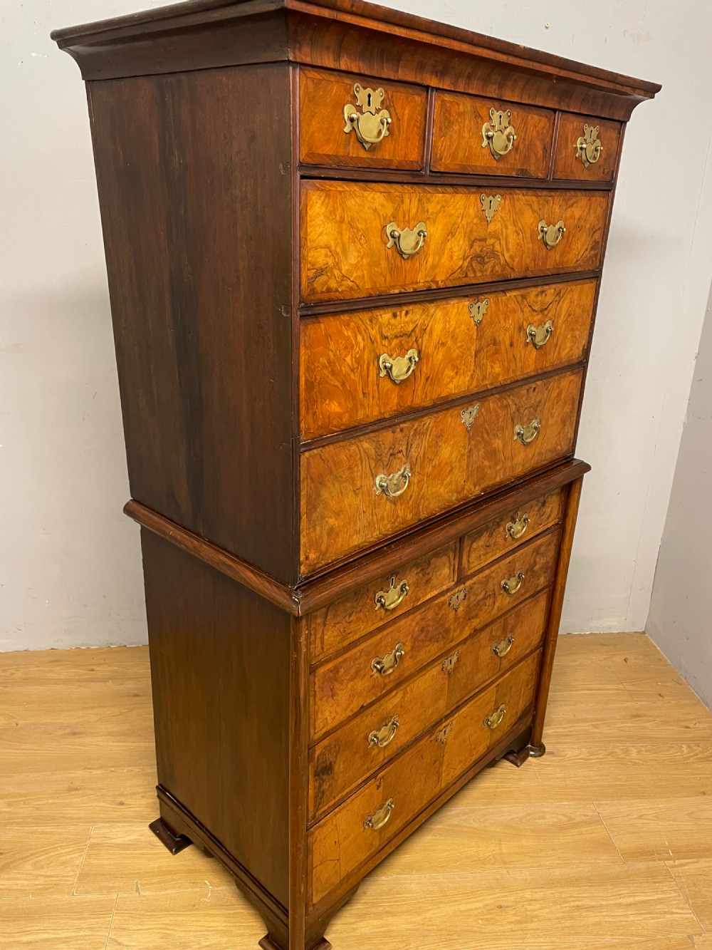 A nineteenth-century burr walnut chest on chest with multiple drawers, brass drop handles, keyhole escutcheons, and bracket feet. View XII