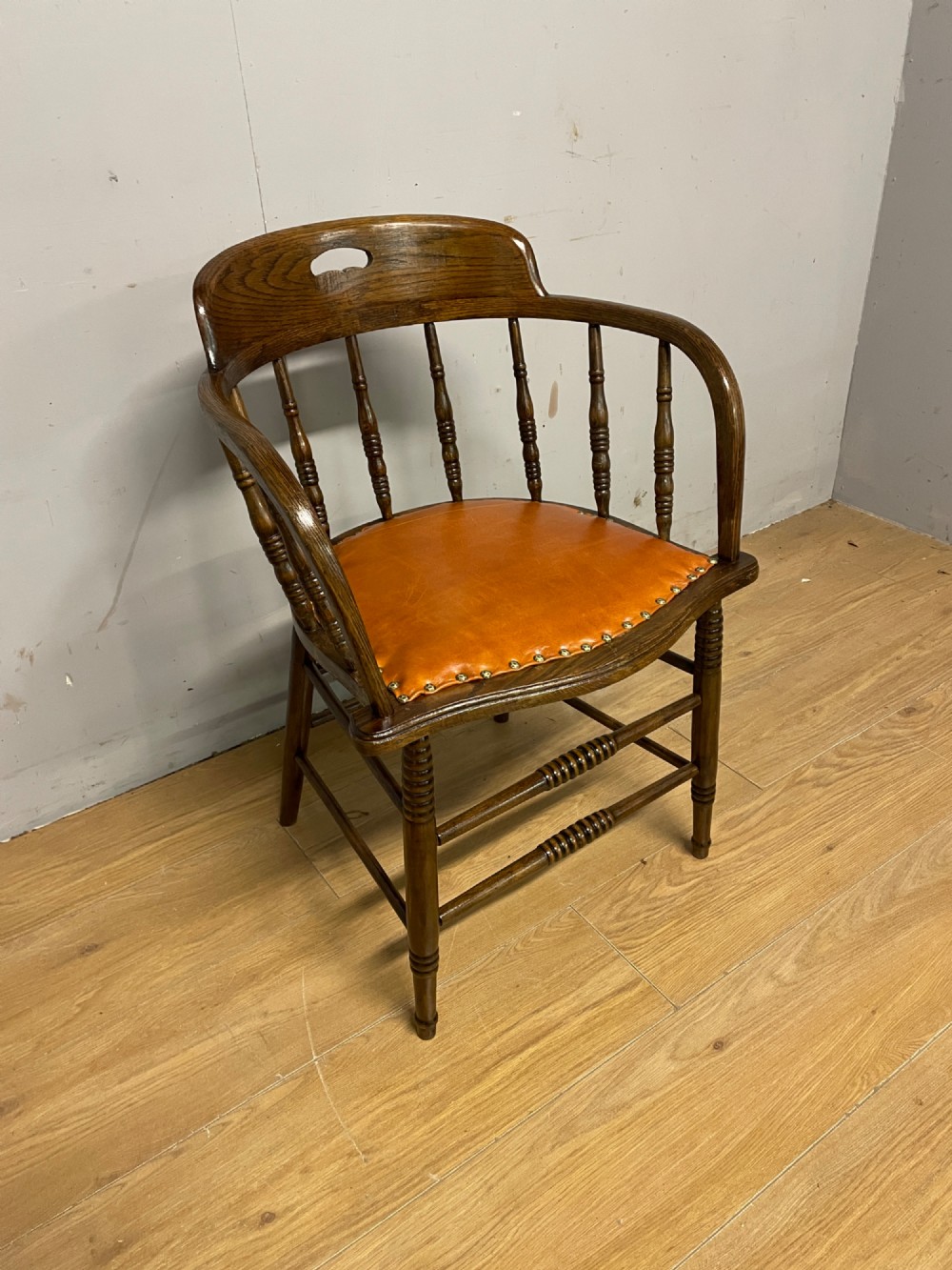 An Edwardian oak and beech desk chair featuring a curved crest rail with a cut-out handle, turned spindles, and a tan leather seat secured with brass studs. View II