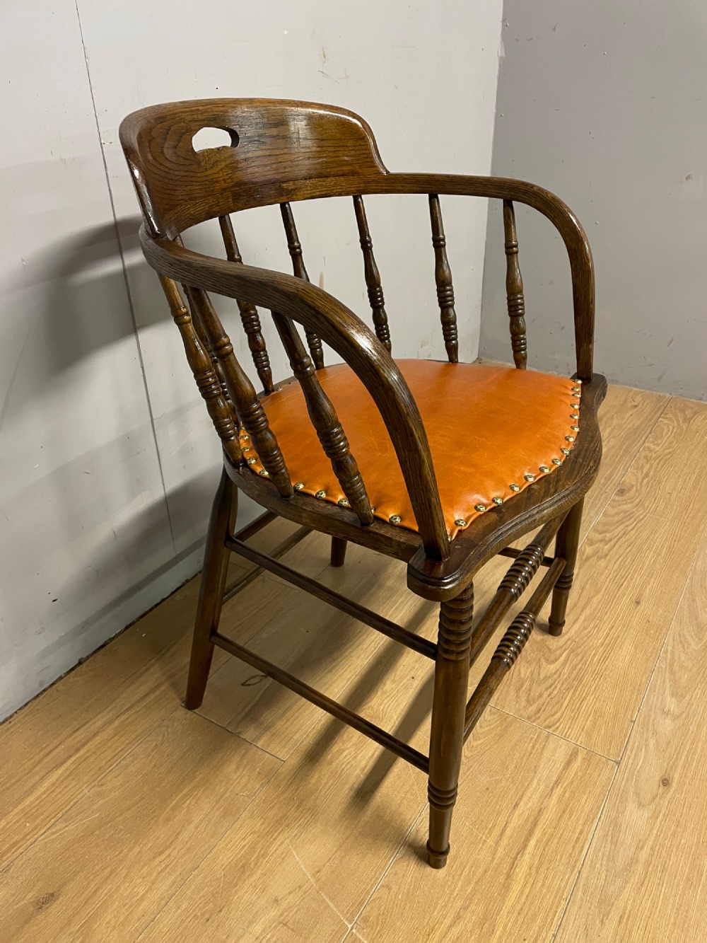 An Edwardian oak and beech desk chair featuring a curved crest rail with a cut-out handle, turned spindles, and a tan leather seat secured with brass studs. View III