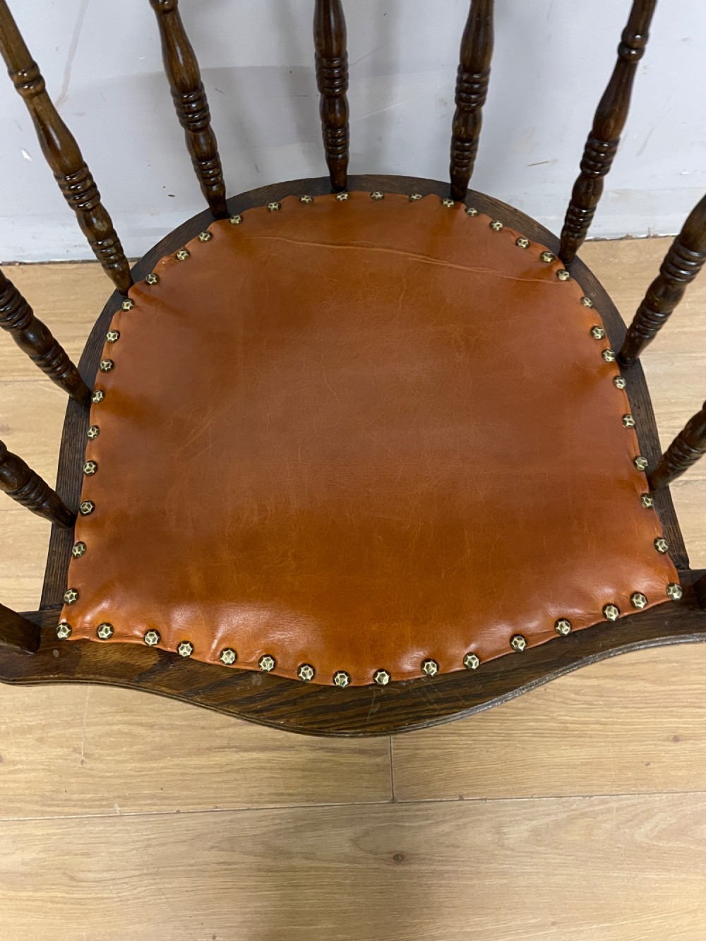An Edwardian oak and beech desk chair featuring a curved crest rail with a cut-out handle, turned spindles, and a tan leather seat secured with brass studs. View IV
