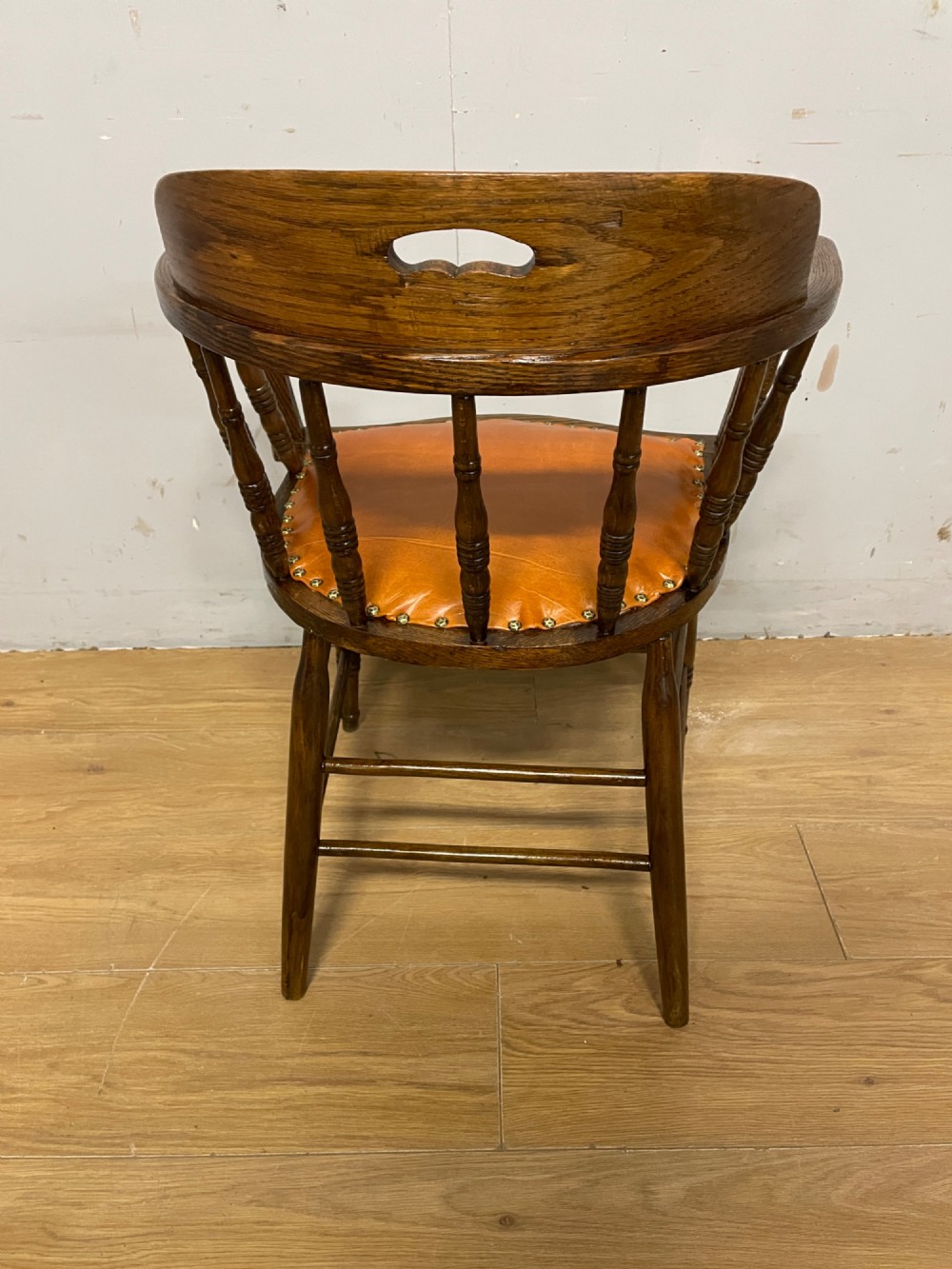 An Edwardian oak and beech desk chair featuring a curved crest rail with a cut-out handle, turned spindles, and a tan leather seat secured with brass studs. View VI