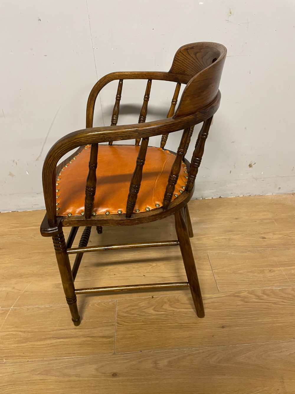 An Edwardian oak and beech desk chair featuring a curved crest rail with a cut-out handle, turned spindles, and a tan leather seat secured with brass studs. View VII
