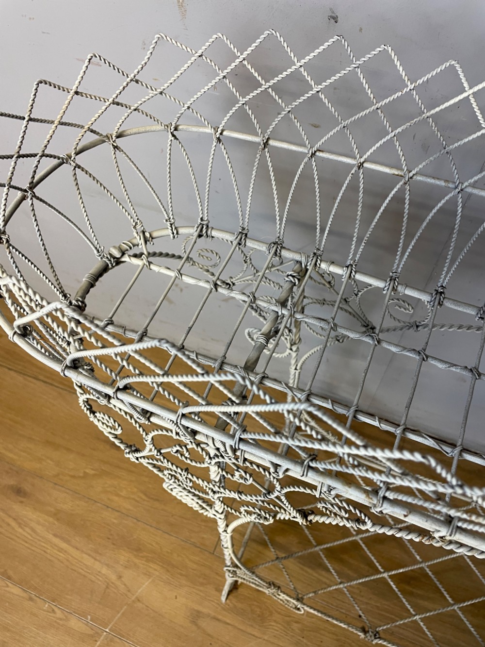A painted distressed white Edwardian wirework plant stand featuring ornate scrollwork, a upper wire lattice basket with a zinc liner, and a lower shelf resting on scroll feet. View XI