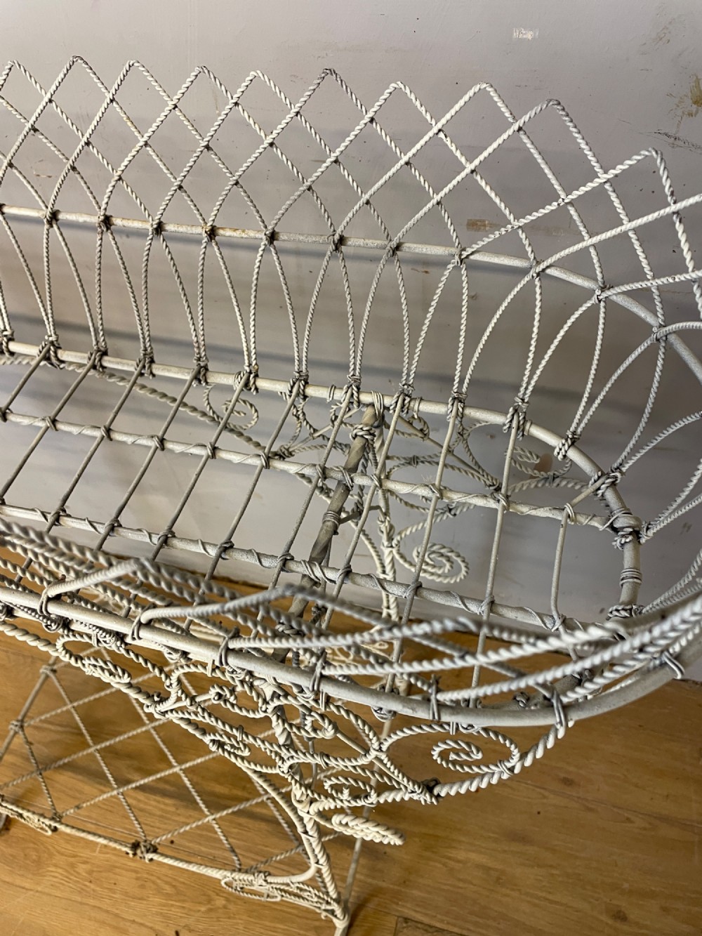 A painted distressed white Edwardian wirework plant stand featuring ornate scrollwork, a upper wire lattice basket with a zinc liner, and a lower shelf resting on scroll feet. View XII