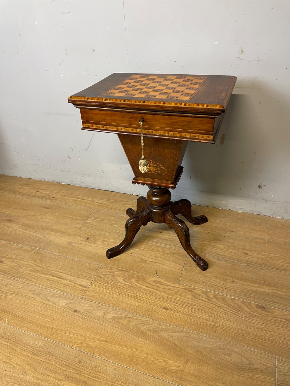 A 19th-century Victorian walnut sewing and games table featuring an inlaid chessboard top, a tapered central storage well, and a carved pedestal base.