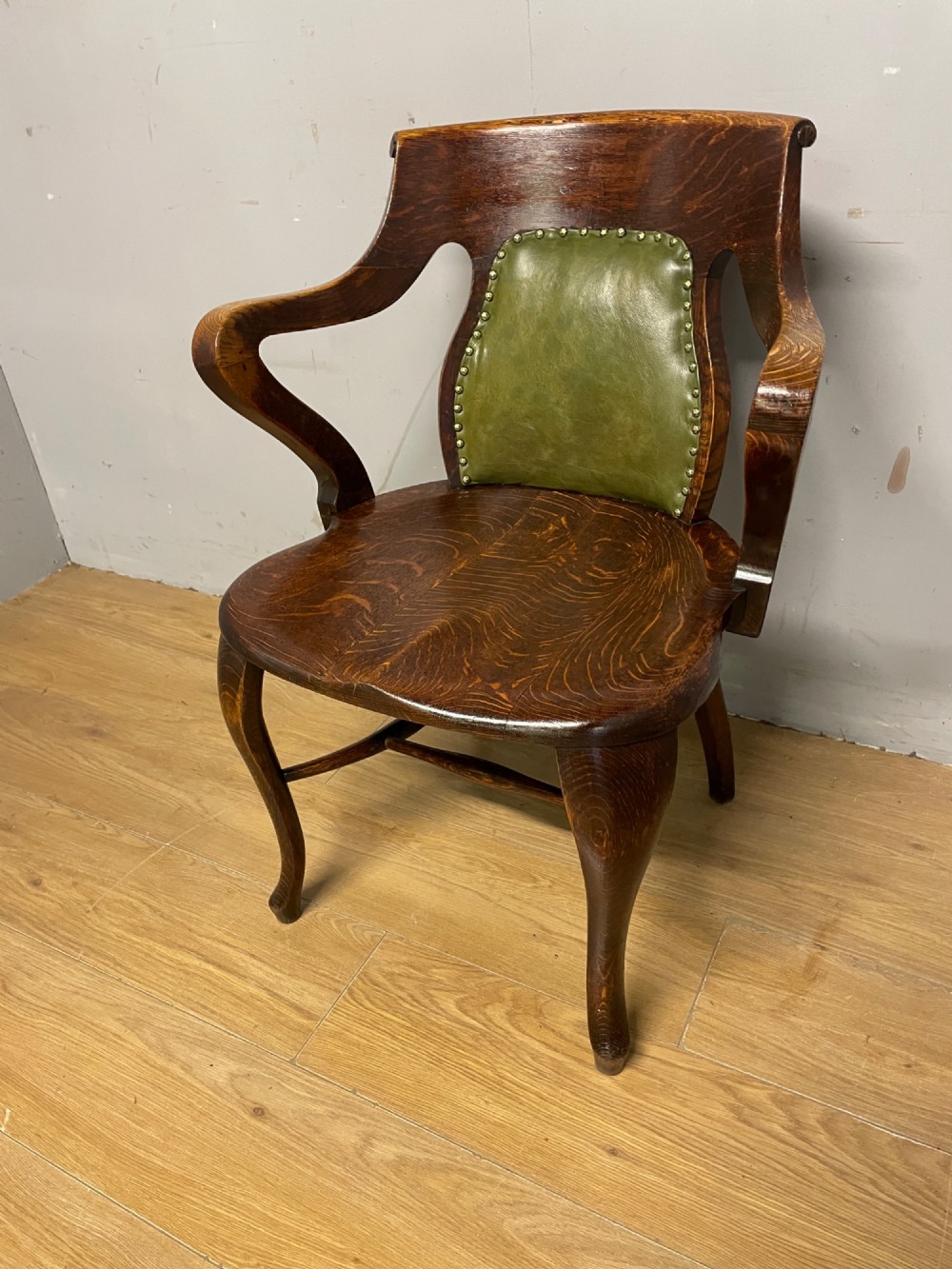 Late nineteenth-century solid oak desk chair featuring sweeping arms, a contoured timber seat, and an olive green leather back panel secured with brass studding.