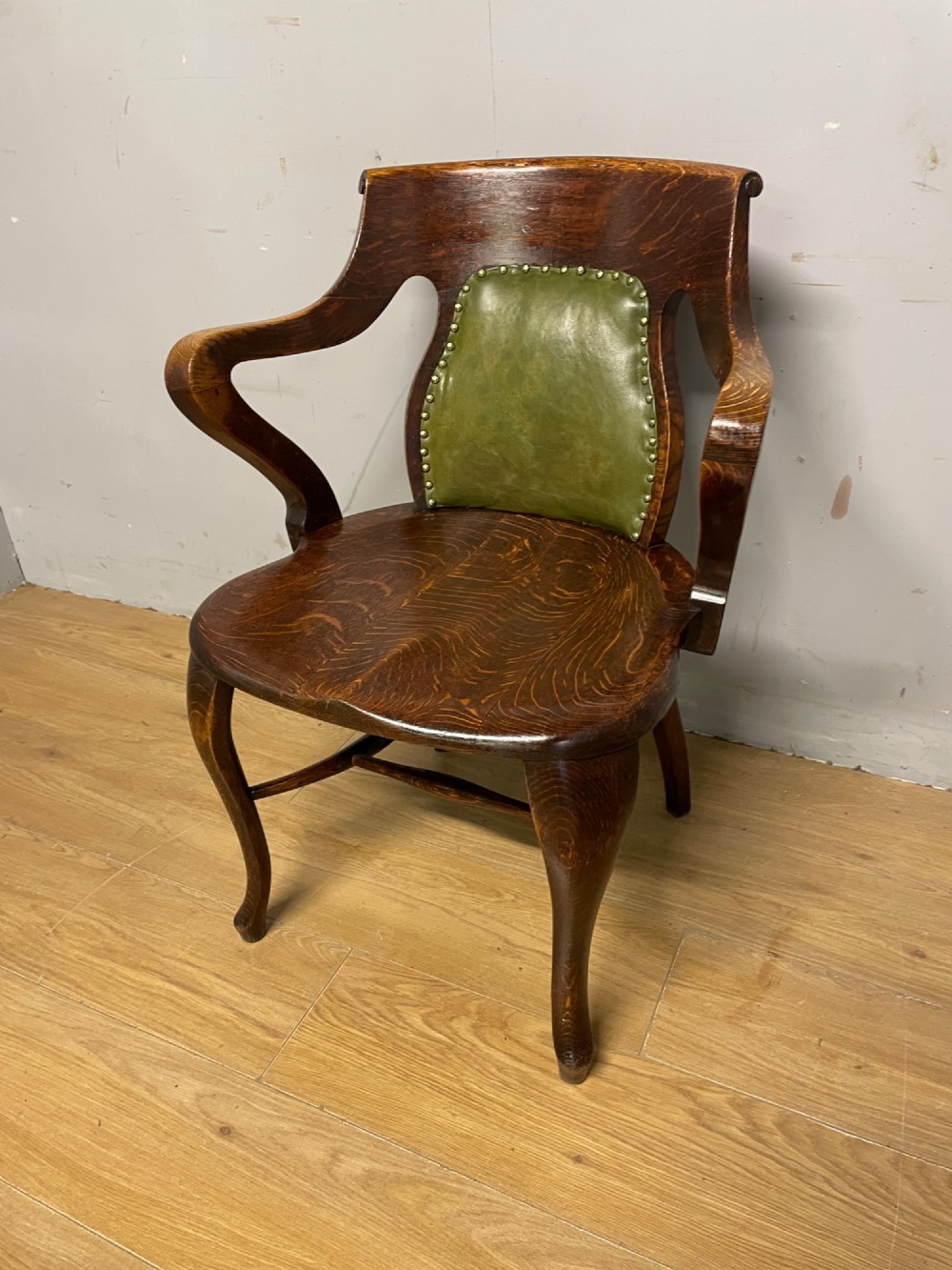 Late nineteenth-century solid oak desk chair featuring sweeping arms, a contoured timber seat, and an olive green leather back panel secured with brass studding. View II