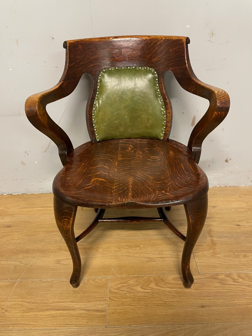 Late nineteenth-century solid oak desk chair featuring sweeping arms, a contoured timber seat, and an olive green leather back panel secured with brass studding. View III