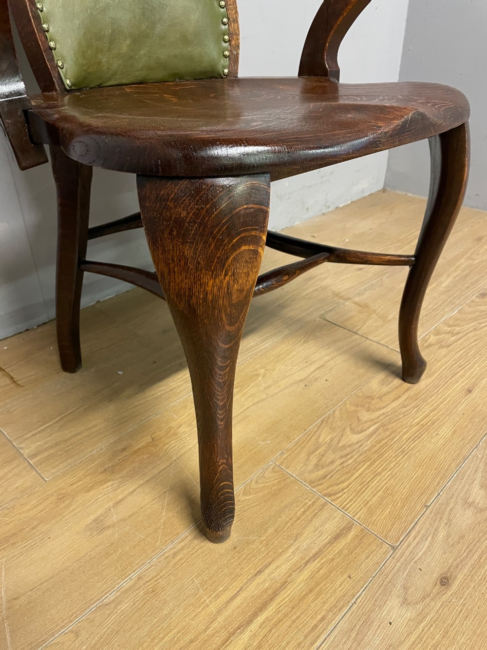 Late nineteenth-century solid oak desk chair featuring sweeping arms, a contoured timber seat, and an olive green leather back panel secured with brass studding. View V