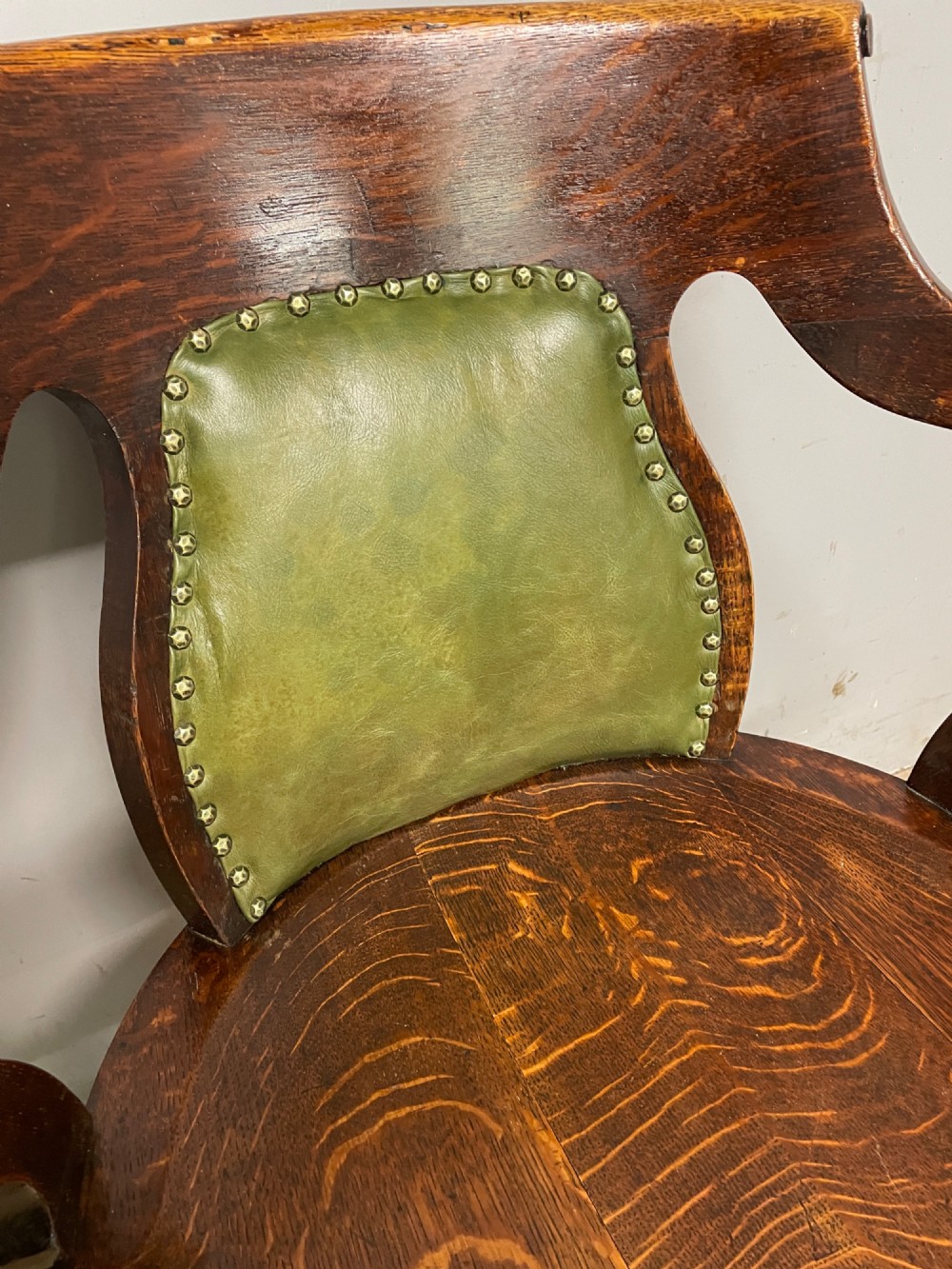 Late nineteenth-century solid oak desk chair featuring sweeping arms, a contoured timber seat, and an olive green leather back panel secured with brass studding. View VI