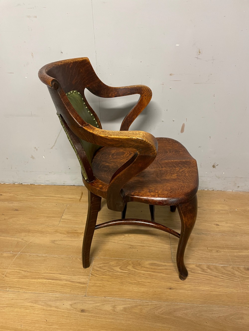 Late nineteenth-century solid oak desk chair featuring sweeping arms, a contoured timber seat, and an olive green leather back panel secured with brass studding. View VII