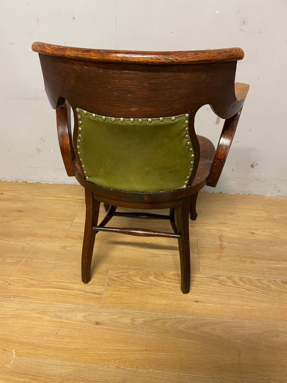 Late nineteenth-century solid oak desk chair featuring sweeping arms, a contoured timber seat, and an olive green leather back panel secured with brass studding. View VIII
