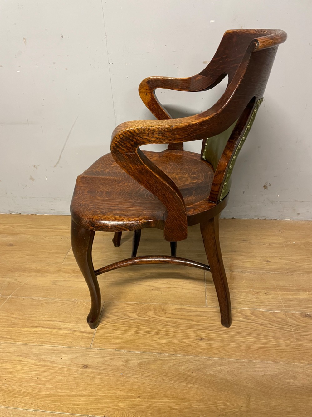Late nineteenth-century solid oak desk chair featuring sweeping arms, a contoured timber seat, and an olive green leather back panel secured with brass studding. View X