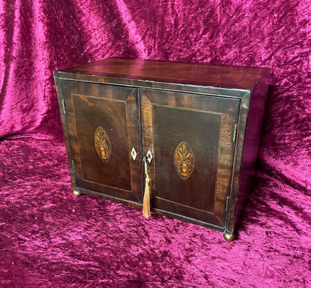 A Georgian dark mahogany tabletop cabinet featuring double doors with oval marquetry urn inlays, diamond escutcheons, and brass ball feet.
