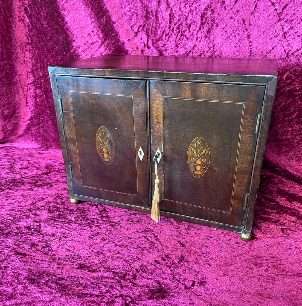 A Georgian dark mahogany tabletop cabinet featuring double doors with oval marquetry urn inlays, diamond escutcheons, and brass ball feet. View II
