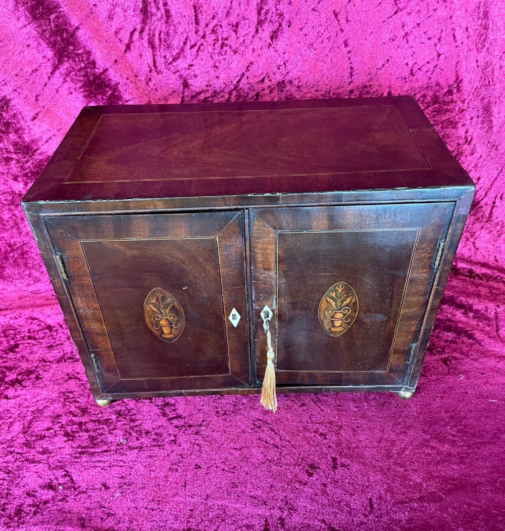 A Georgian dark mahogany tabletop cabinet featuring double doors with oval marquetry urn inlays, diamond escutcheons, and brass ball feet. View III