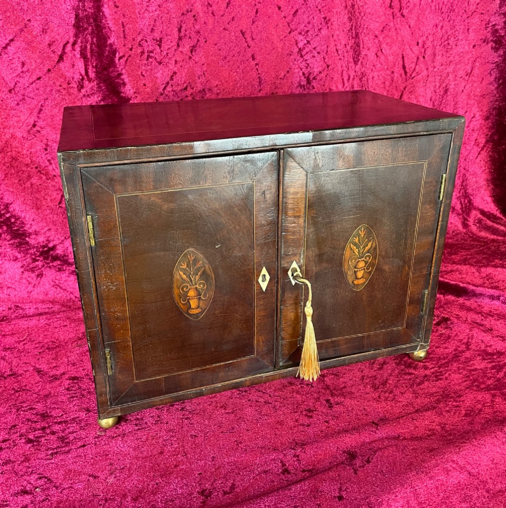 A Georgian dark mahogany tabletop cabinet featuring double doors with oval marquetry urn inlays, diamond escutcheons, and brass ball feet. View XII