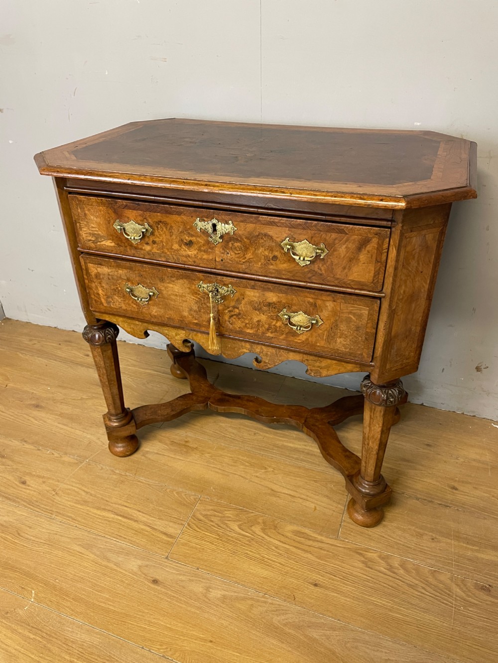 A late Victorian burr walnut lowboy featuring two drawers with brass handles, carved legs, and a shaped cross-stretcher.