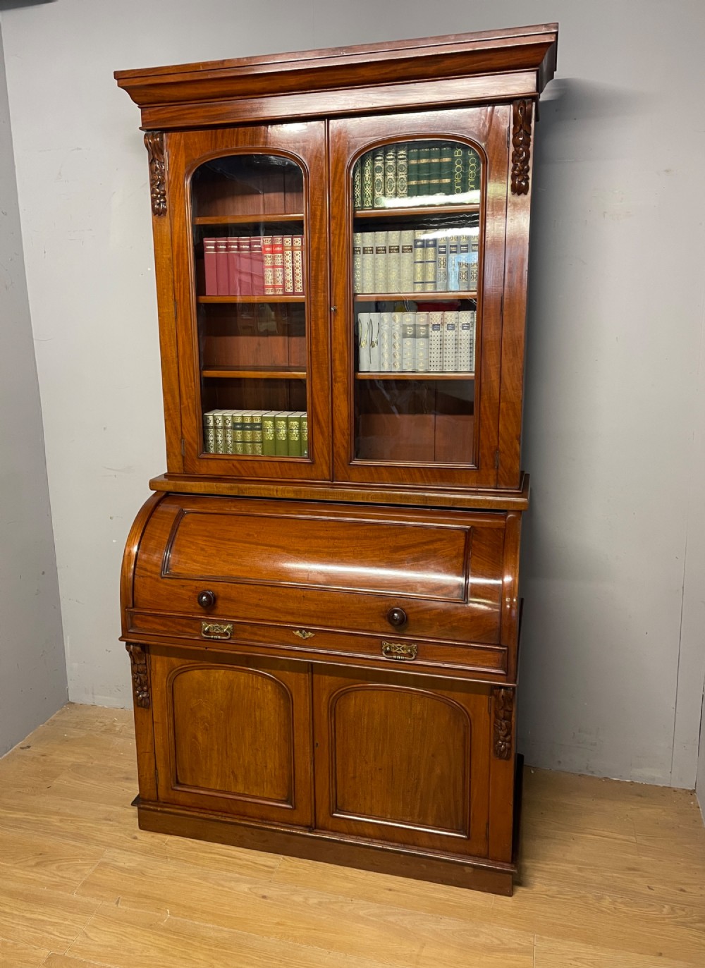 A 19th-century mahogany cylinder bureau bookcase featuring an upper glazed cabinet with two arched doors, a roll-top writing section, and a lower two-door cupboard.