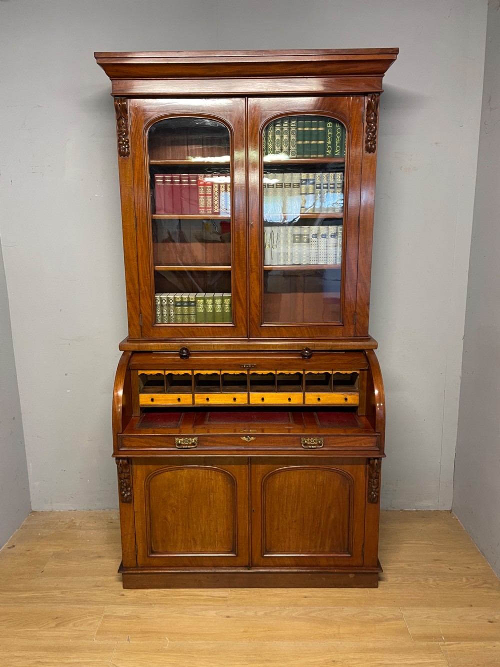 A 19th-century mahogany cylinder bureau bookcase featuring an upper glazed cabinet with two arched doors, a roll-top writing section, and a lower two-door cupboard. View II